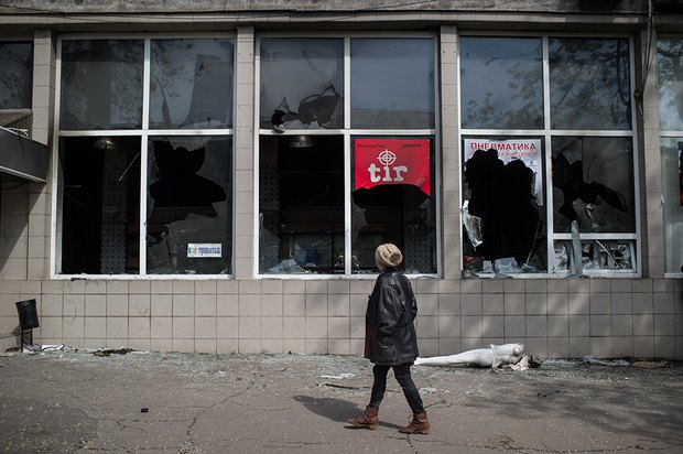 Женщина проходит мимо разбитых витрин магазина оружия в Мариуполе