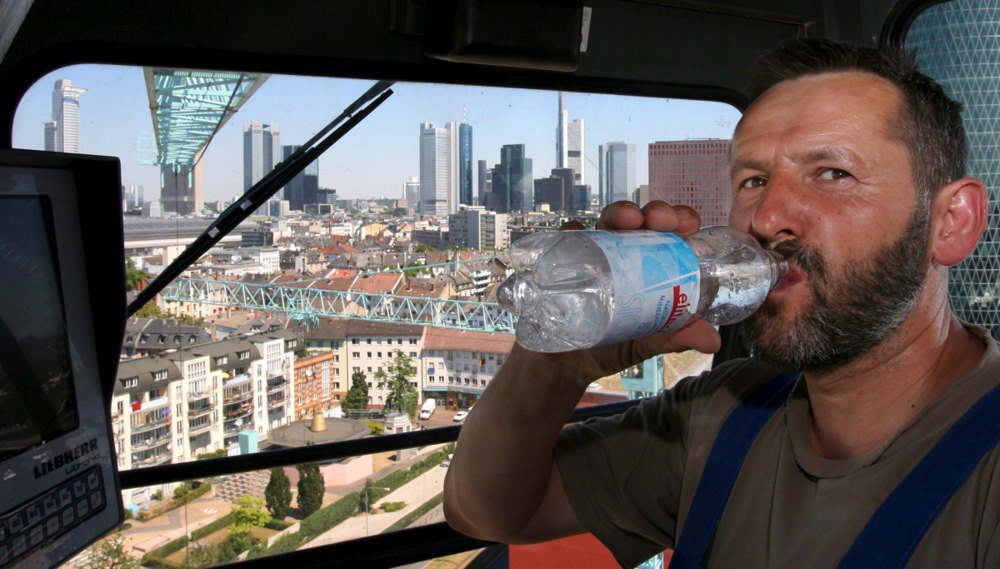 Кранівник п’є воду в кабіні, де немає кондиціонування, спекотного робочого дня, Франкфурт, Німеччина