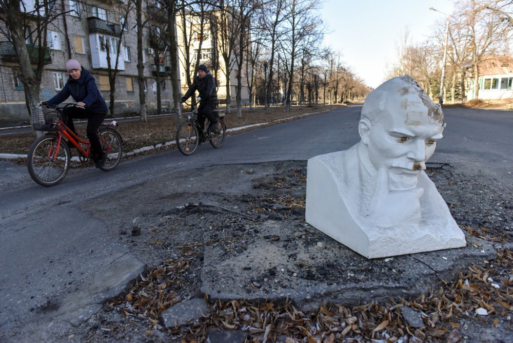 Місцеві мешканці проїжджають повз знесений бюст Леніна, який закриває яму на дорозі в місті Лиман Донецької області, 26 січня 2023 року.