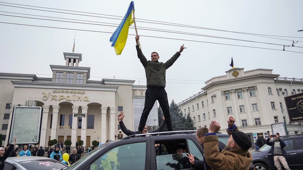 Чоловік з прапором України стоїть на авто, люди святкують звільнення міста від Росії. Херсон, 12 листопада 2022 року.