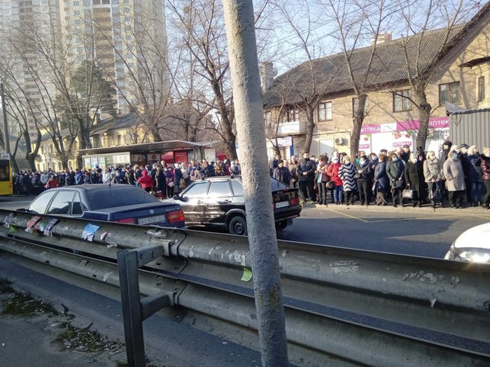 На зупинці поруч зі станцією метро «Чернігівська» автобуса чекає кілька десятків осіб