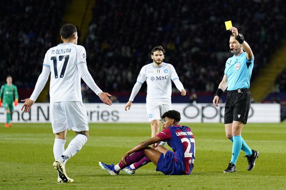  Арбітр Денні Маккеле (праворуч) показує жовту картку Матіасу Олівері ‘Наполі’ (ліворуч), під час матчу-відповіді 1/8 фіналу Ліги чемпіонів УЄФА в Барселоні. Ламін Ямал ‘Барселона’ сидить на полі у центрі.