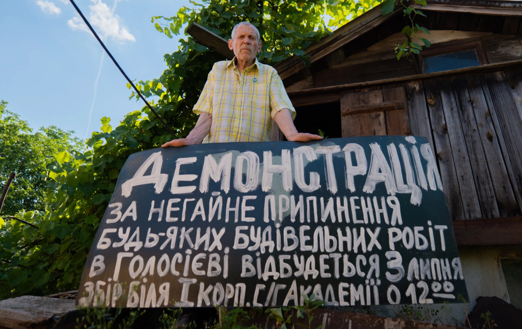 Михайло Михалко. Ековетеран біля щита з анонсом дати і часу демонстрації на захист Голосіївського лісу