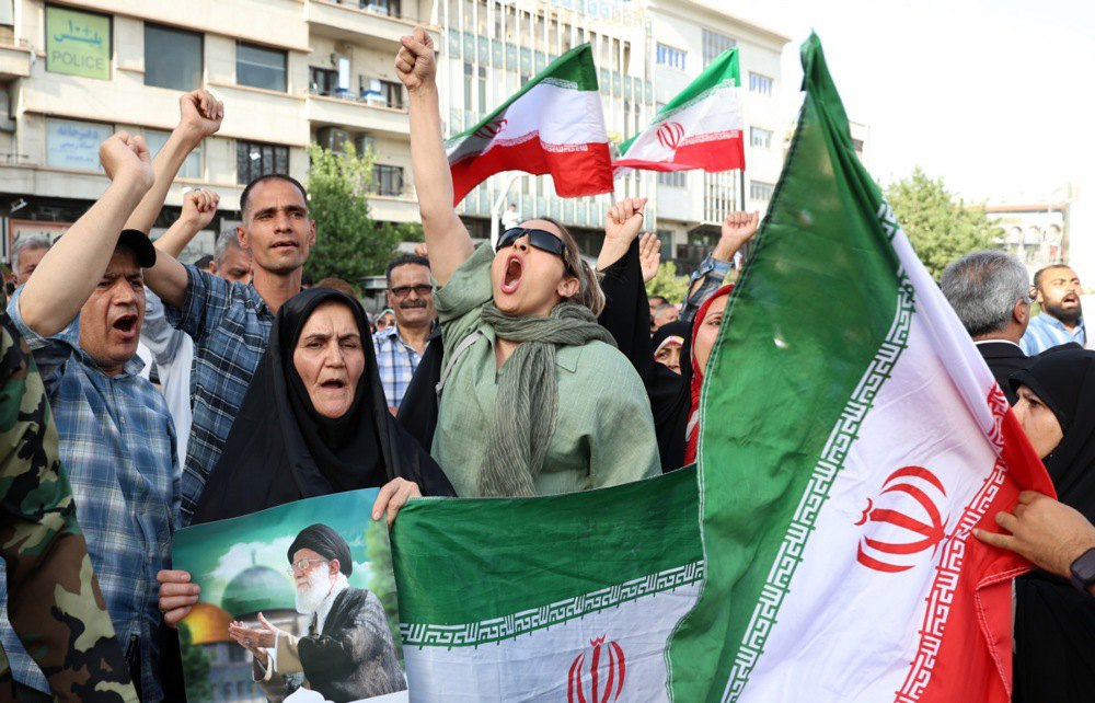 Іранці з національними прапорами та плакатом із зображенням Верховного лідера Ірану аятоли Алі Хаменеї під час антиамериканської
та антиізраїльської акції в Тегерані, 22 червня 2025 року.