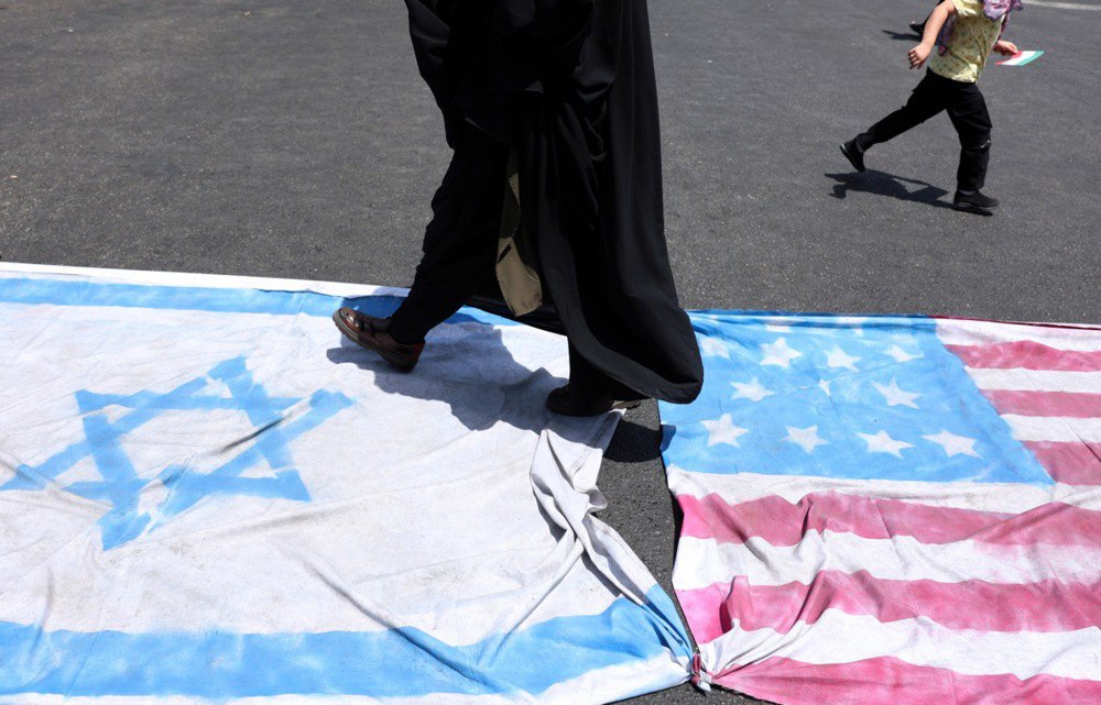 Протестувальниця йде по прапорах Ізраїлю та США під час мітингу в Тегерані, 20 червня 2025 року.