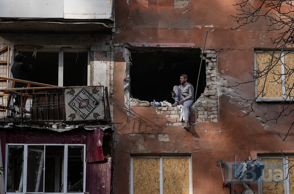 Чоловік сидить у вікні, вибитому внаслідок обстрілу будинку