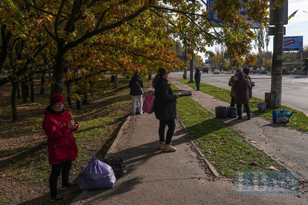 Люди ховаються під деревами на автобусній зупинці.