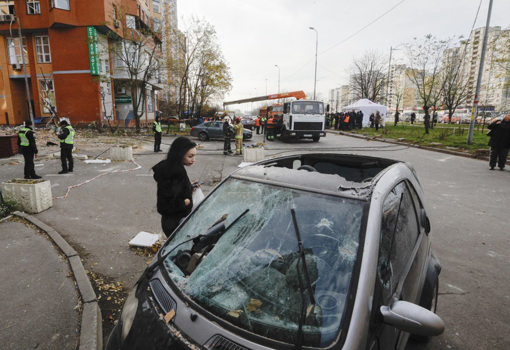 Жінка оглядає свій пошкоджений автомобіль на місці обстрілу в Києві, 14 листопада 2025 року.