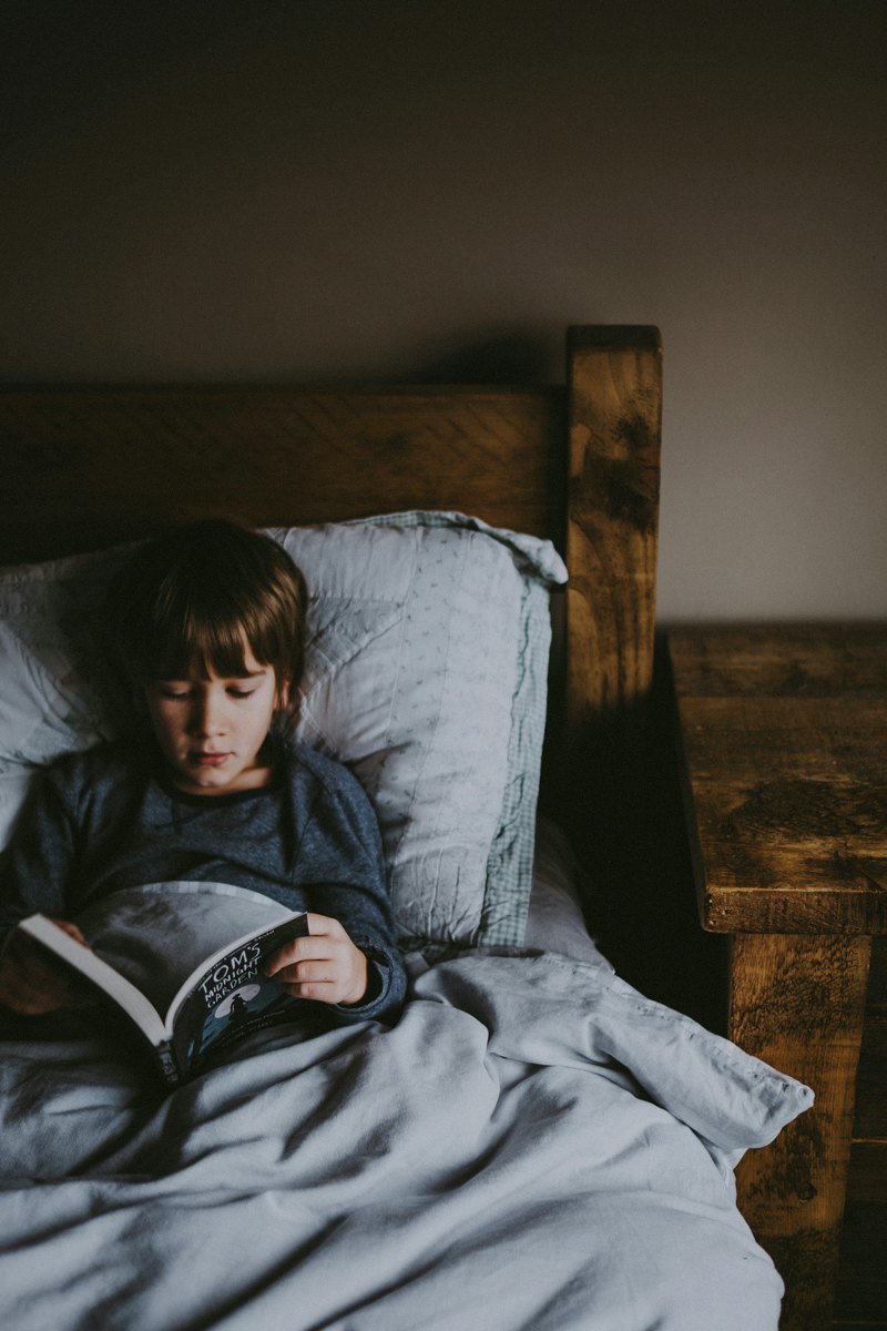 Хлопчик читає книжку в ліжку.