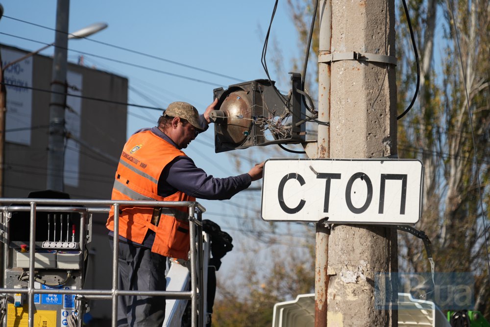 Комунальник знімає побитий уламками світлофор.