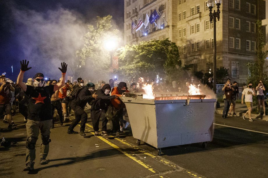 Демонстранты толкают горящий мусорник навстречу полиции во время протестов возле Белого дома в Вашингтоне, 30 мая 2020.