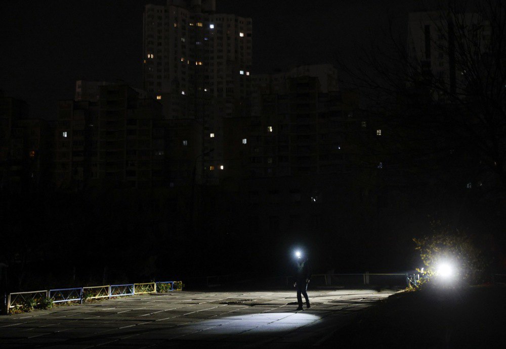 Людина йде з ліхтариком неосвітленою вулицею під час відключення електроенергії в Києві.