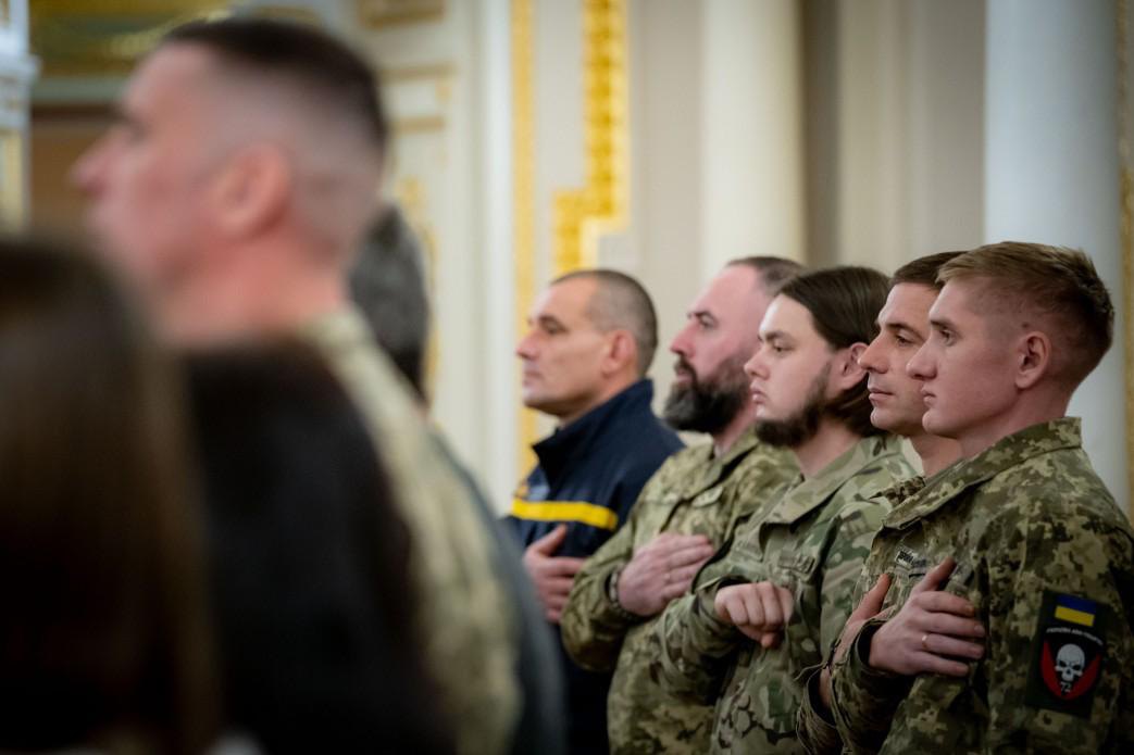 Військовослужбовці та цивільні учасники церемонії стоять із рукою на серці під час офіційного заходу