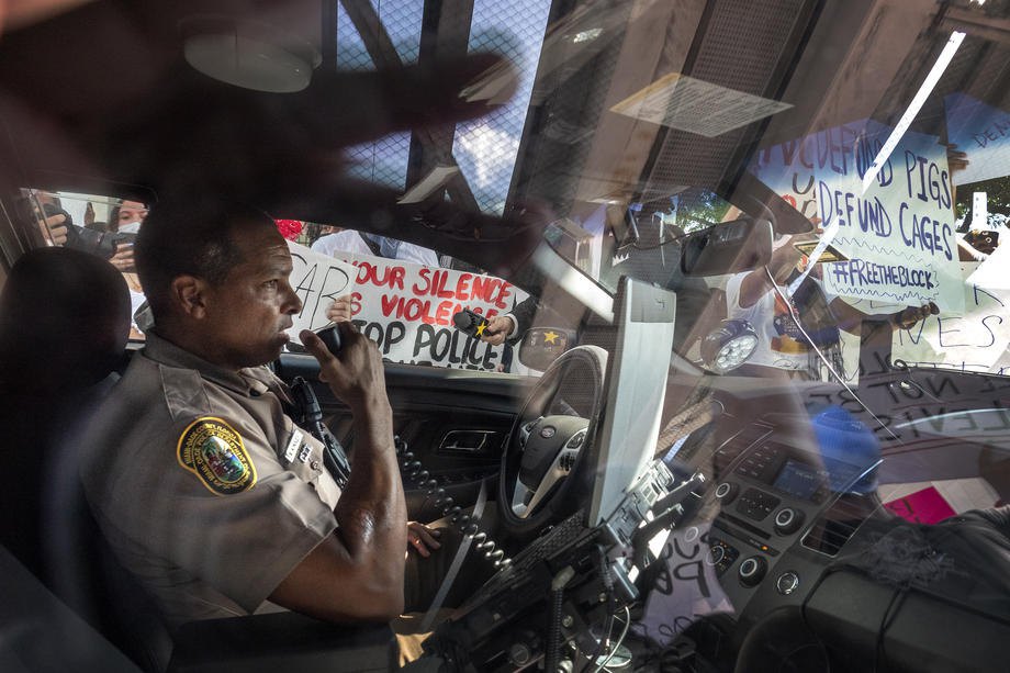 Офицер департамента полиции Майами в своей машине в окружении протестующих, во время протестов в Майами, Флорида, 30 мая 2020 