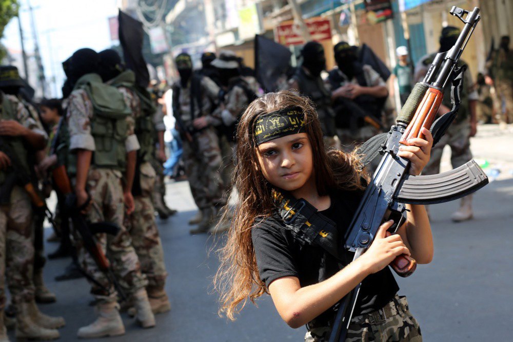 A Palestinian girl holds a Kalashnikov rifle next to Hamas militants, Gaza, 29 August 2014