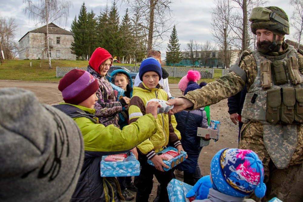 Volunteers and Ukrainian soldiers hand out sweets to children in recently liberated Kupyansk, Kharkiv Region