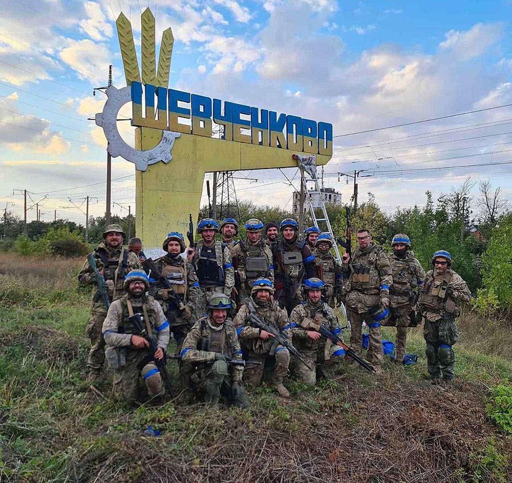  Territorial Defence soldiers beside a freshly repainted entrance sign in Shevchenkove, changed from the colours of the Russian tricolour to the blue and yellow of the Ukrainian flag, after the settlement was liberated from the Russian army